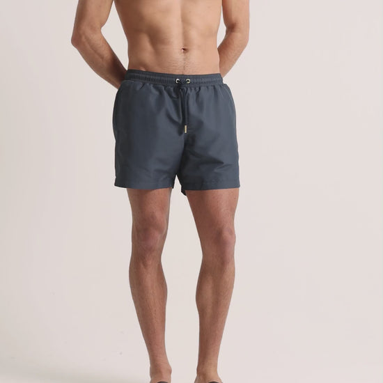 Man wearing grey swim shorts on a plain background
