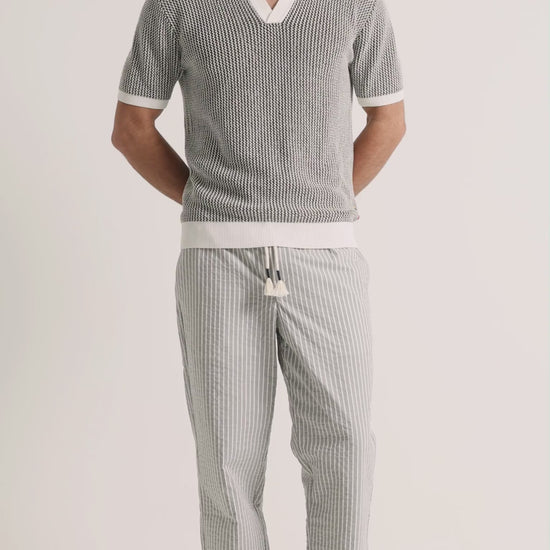 Man wearing crochet light green polo shirt with grey striped trousers on a plain background