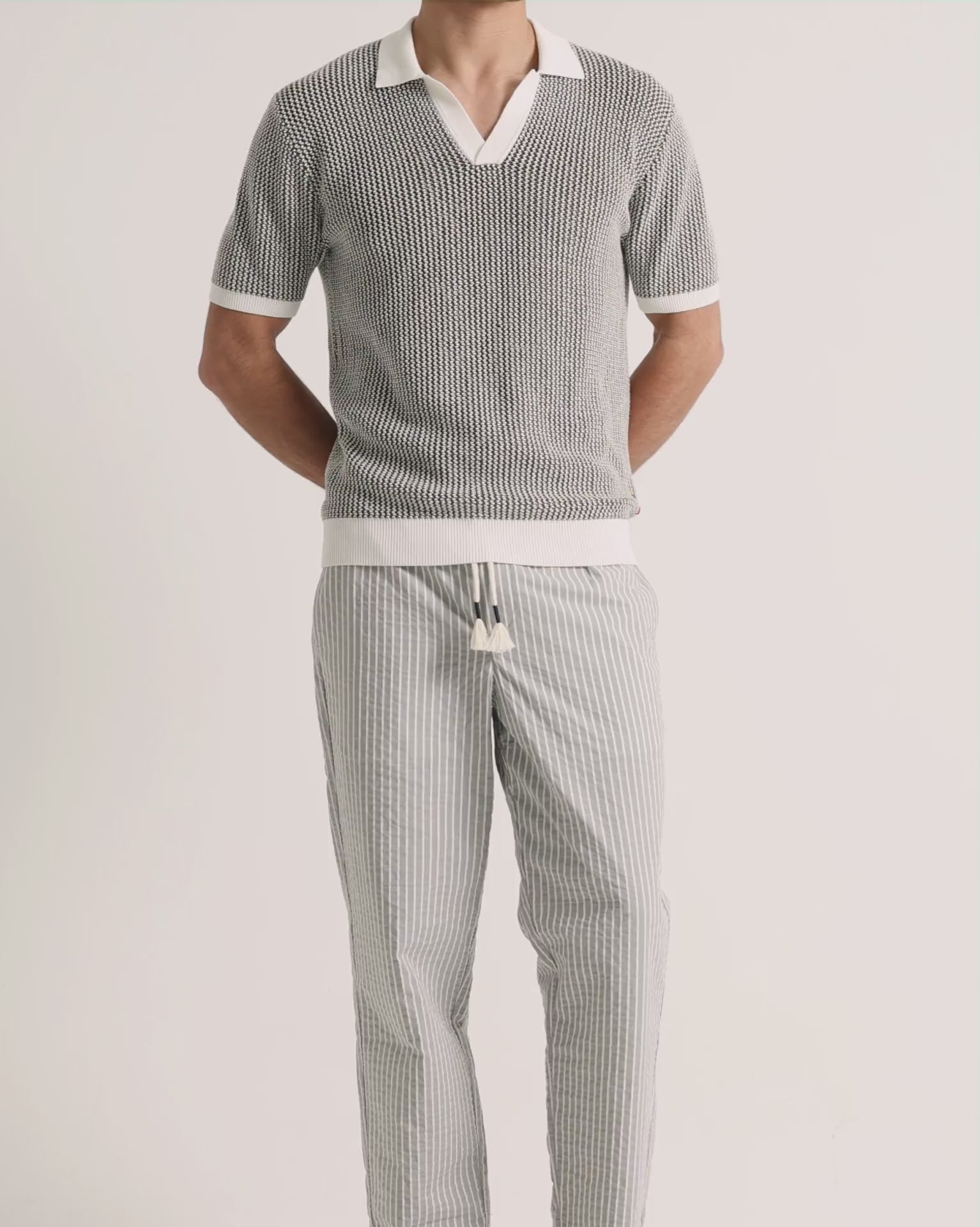 Man wearing crochet light green polo shirt with grey striped trousers on a plain background