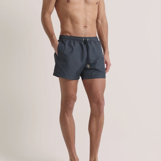 Man wearing grey swim shorts on a plain background
