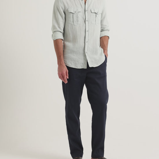 Man wearing Ray linen navy tailored trousers with pale blue shirt with chest pockets