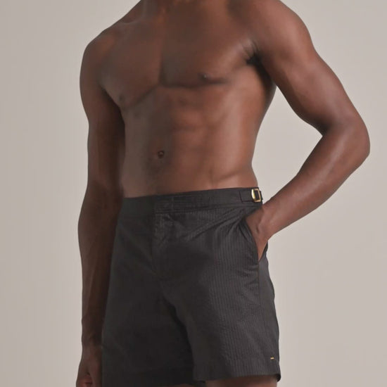 Man wearing dark brown seersucker swim shorts on a plain background