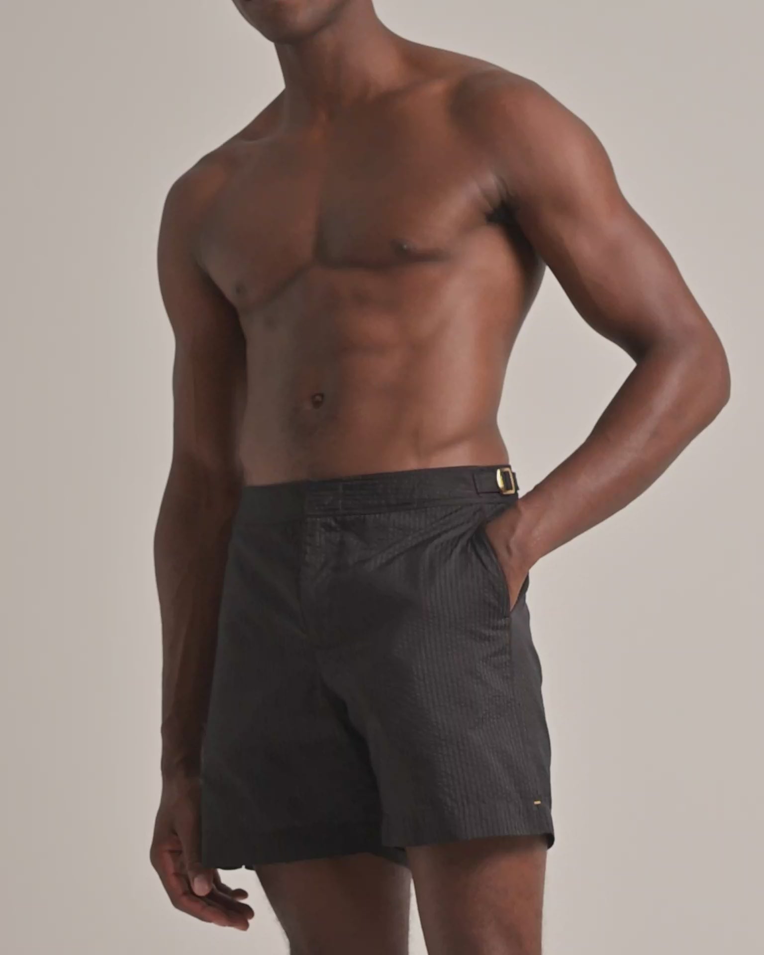 Man wearing dark brown seersucker swim shorts on a plain background
