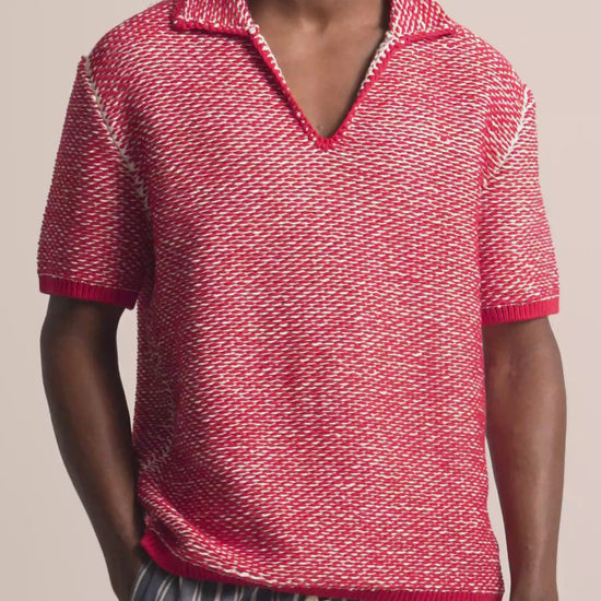 Man wearing red and white crochet stitch polo shirt with navy and white striped trousers against a plain background