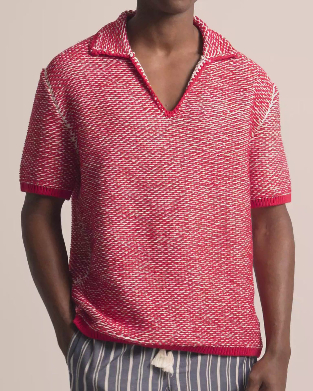 Man wearing red and white crochet stitch polo shirt with navy and white striped trousers against a plain background