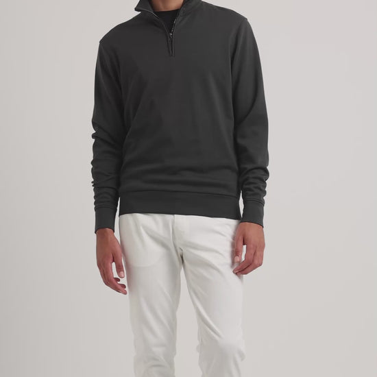 Man wearing black quarter-zip sweatshirt with white trousers on a plain background