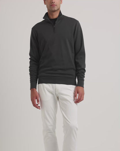 Man wearing black quarter-zip sweatshirt with white trousers on a plain background