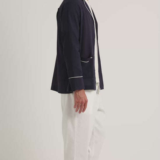 Man wearing navy jacket with white trim with white t-shirt and trousers on a plain background