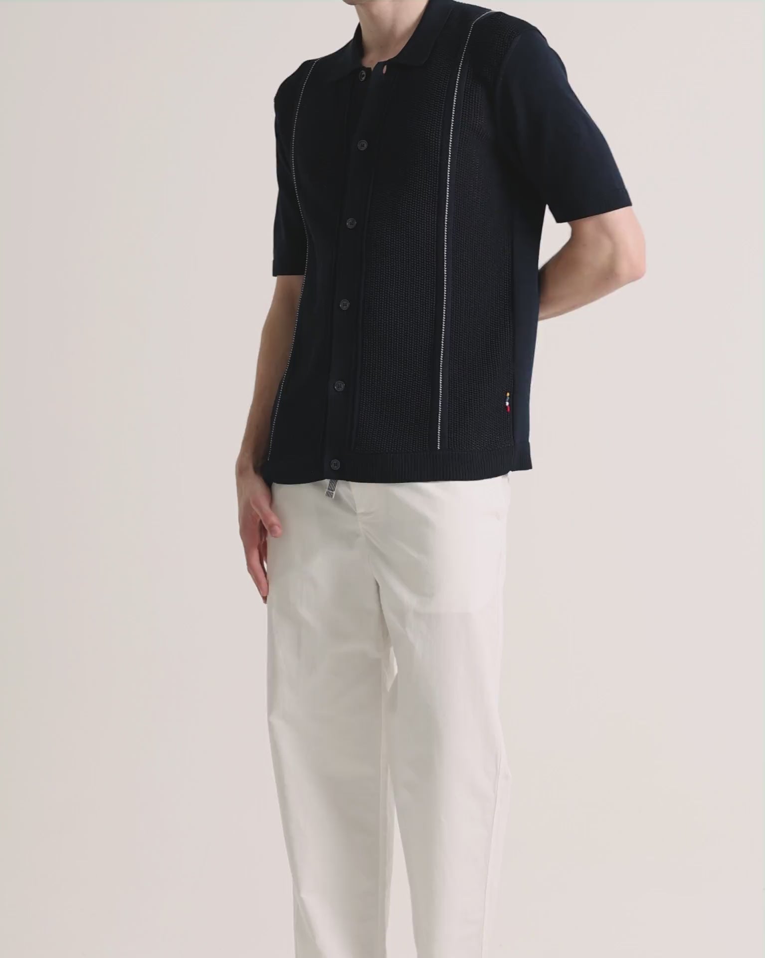 Man wearing navy knitted shirt with white trousers on a plain background
