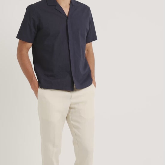 Man wearing a navy short sleeve shirt with beige trousers on a plain background