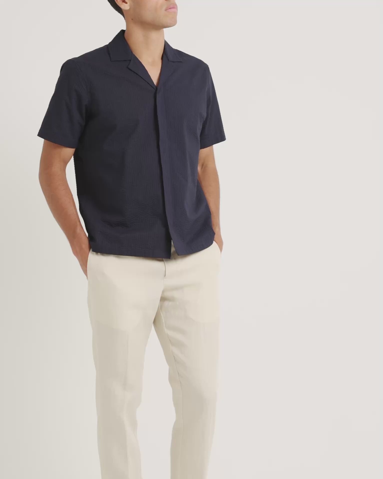 Man wearing a navy short sleeve shirt with beige trousers on a plain background