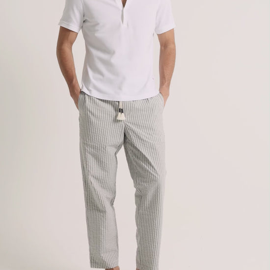 Man wearing white polo shirt with grey striped trousers on a plain background