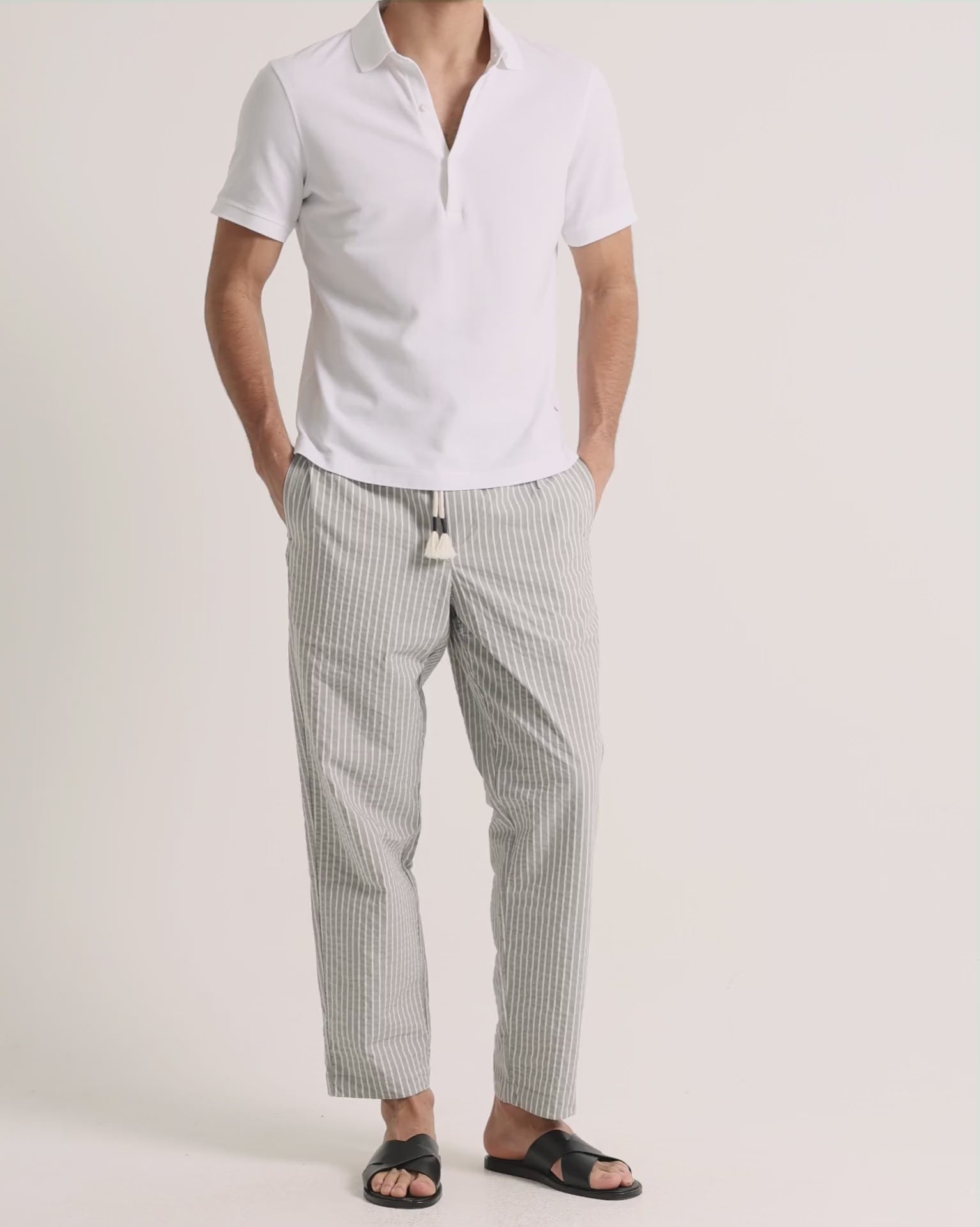 Man wearing white polo shirt with grey striped trousers on a plain background