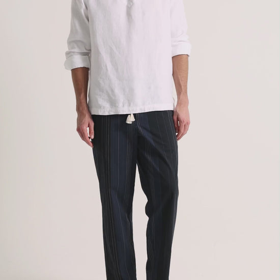 Man wearing white linen shirt with navy trousers on a plain background