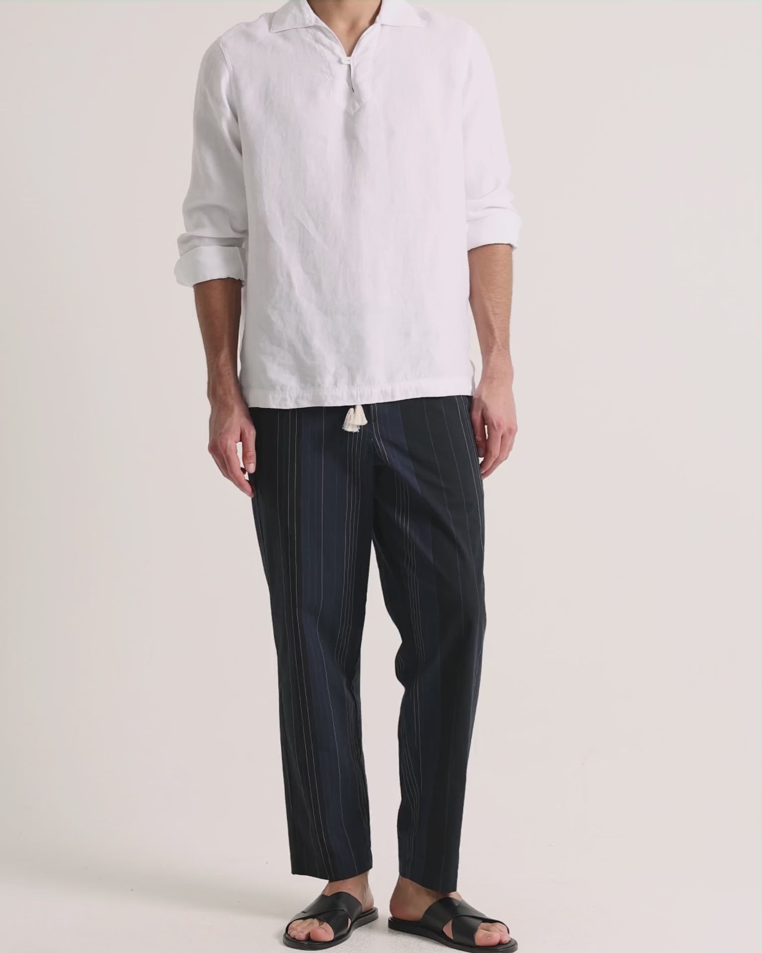 Man wearing white linen shirt with navy trousers on a plain background