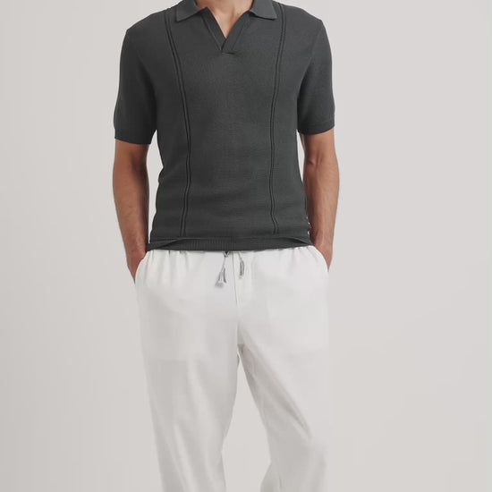 Man wearing a grey polo shirt with white drawstring trousers on a plain background