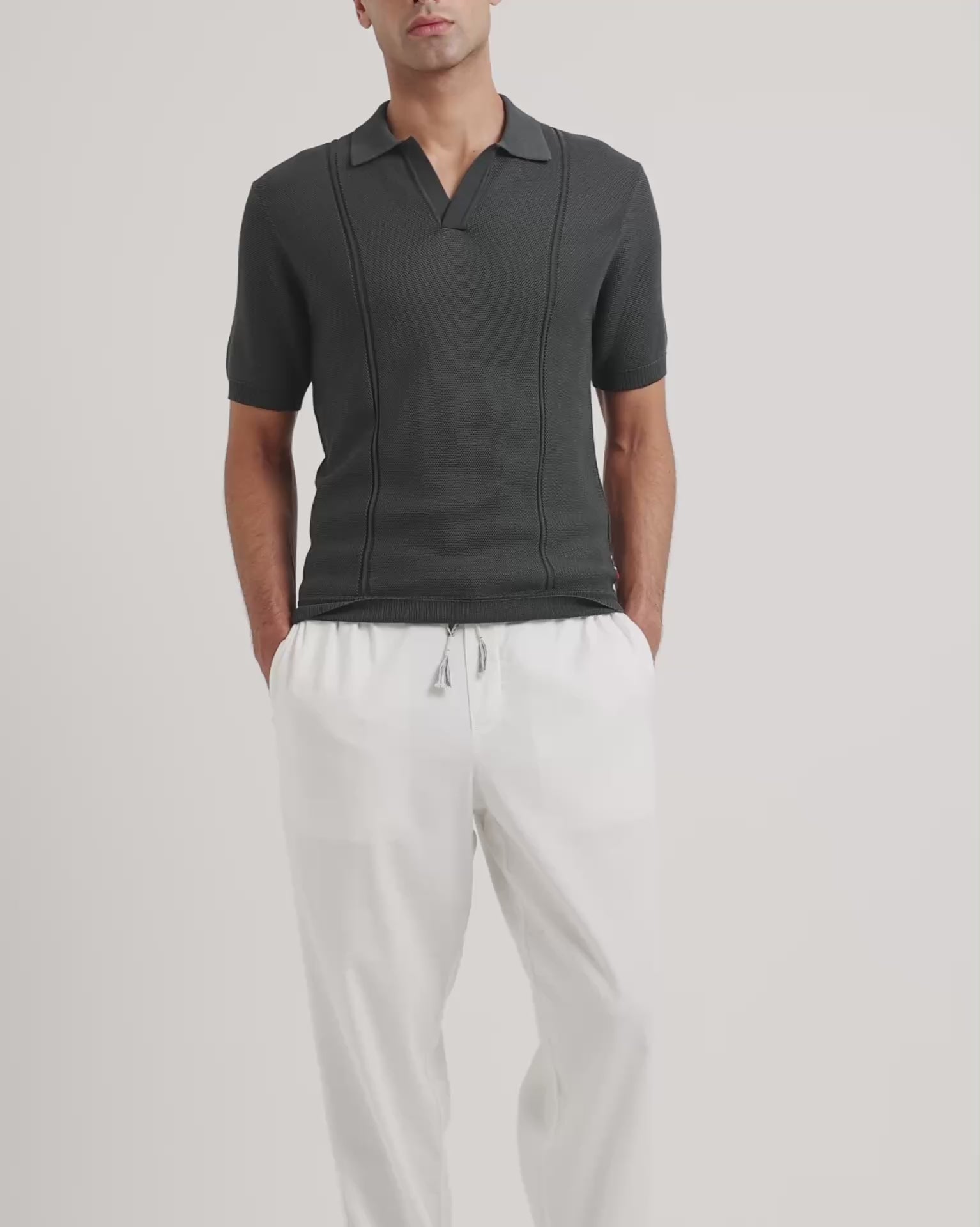 Man wearing a grey polo shirt with white drawstring trousers on a plain background