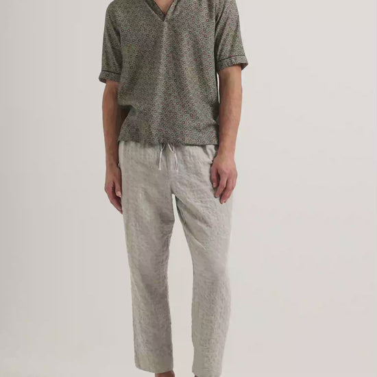 Video of model wearing printed short sleeve shirt with grey trousers on a plain background