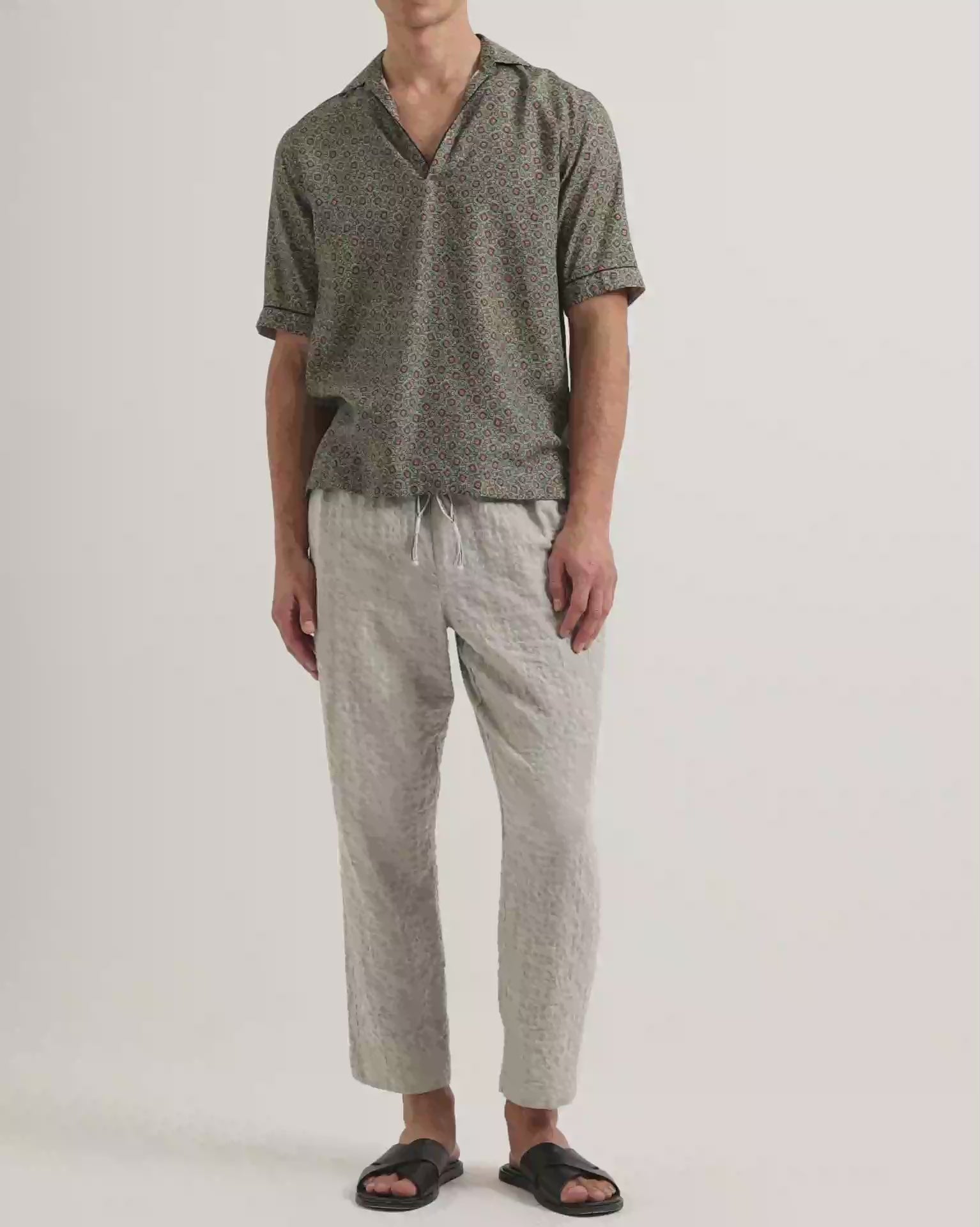 Video of model wearing printed short sleeve shirt with grey trousers on a plain background