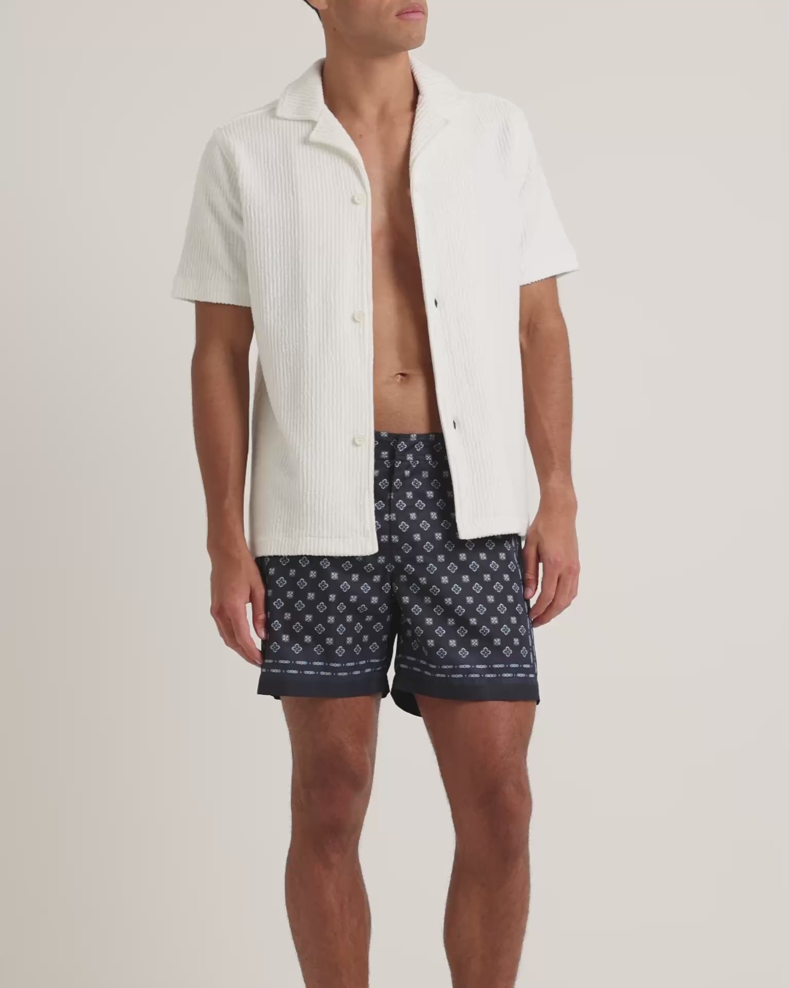 Man wearing textured white shirt with navy geometric print shorts on a plain background