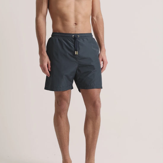Man wearing grey swim shorts on a plain background