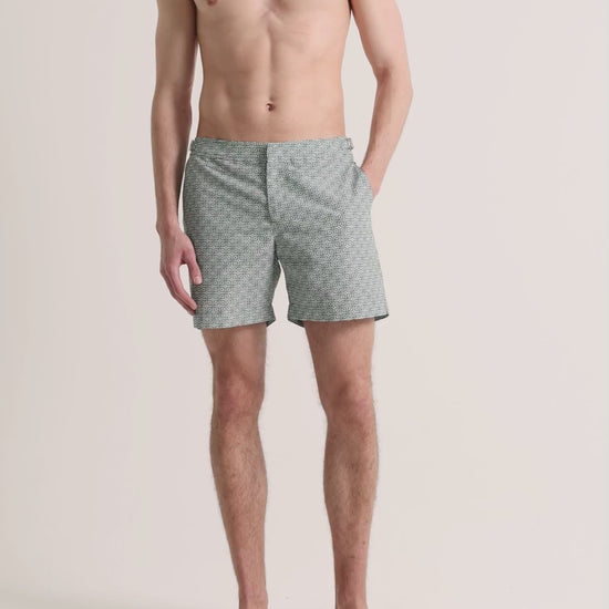Man wearing green printed swim shorts on a plain background