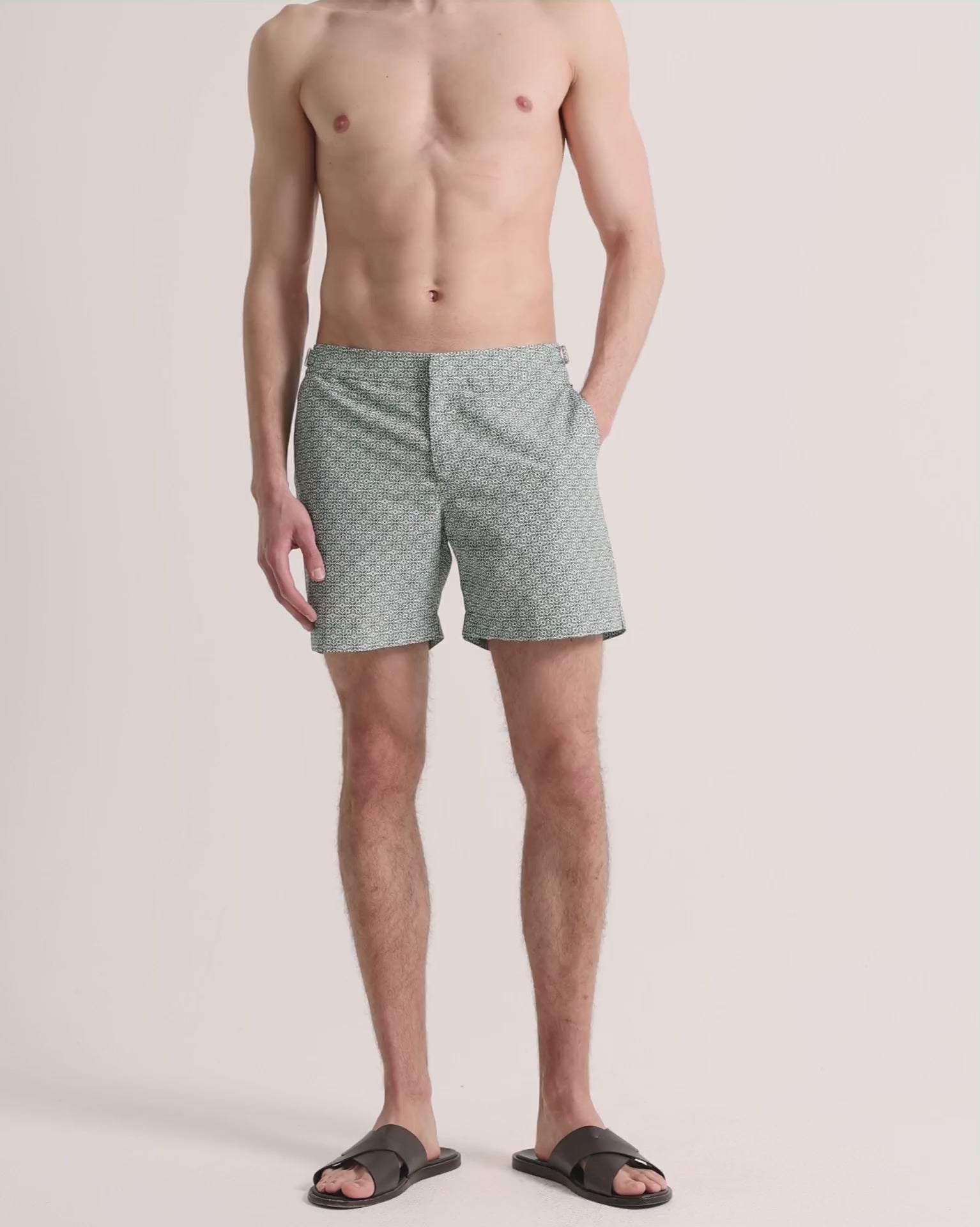 Man wearing green printed swim shorts on a plain background