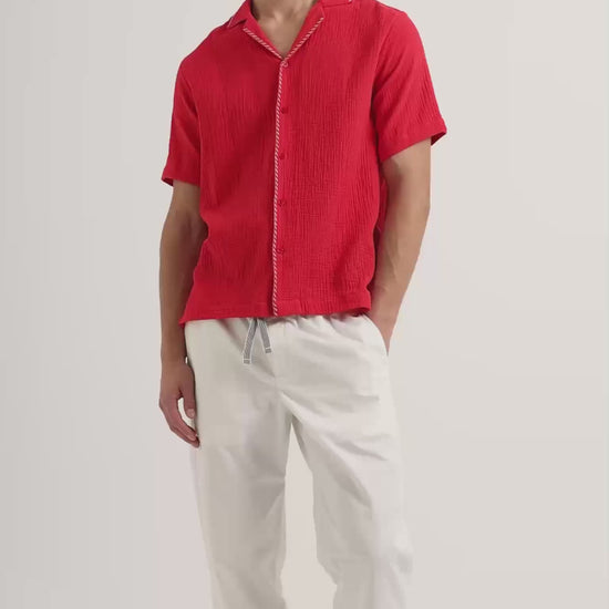 Man wearing red short sleeve shirt with white tipping and white drawstring trousers