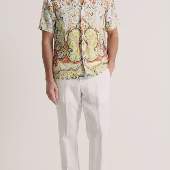Man wearing printed linen shirt with white trousers on a plain background