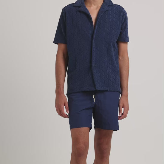 Man wearing navy towelling shirt with navy drawcord swim shorts on a plain background