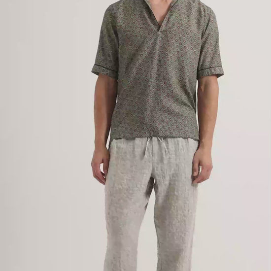 Man wearing patterned short sleeve shirt in green with light grey linen trousers