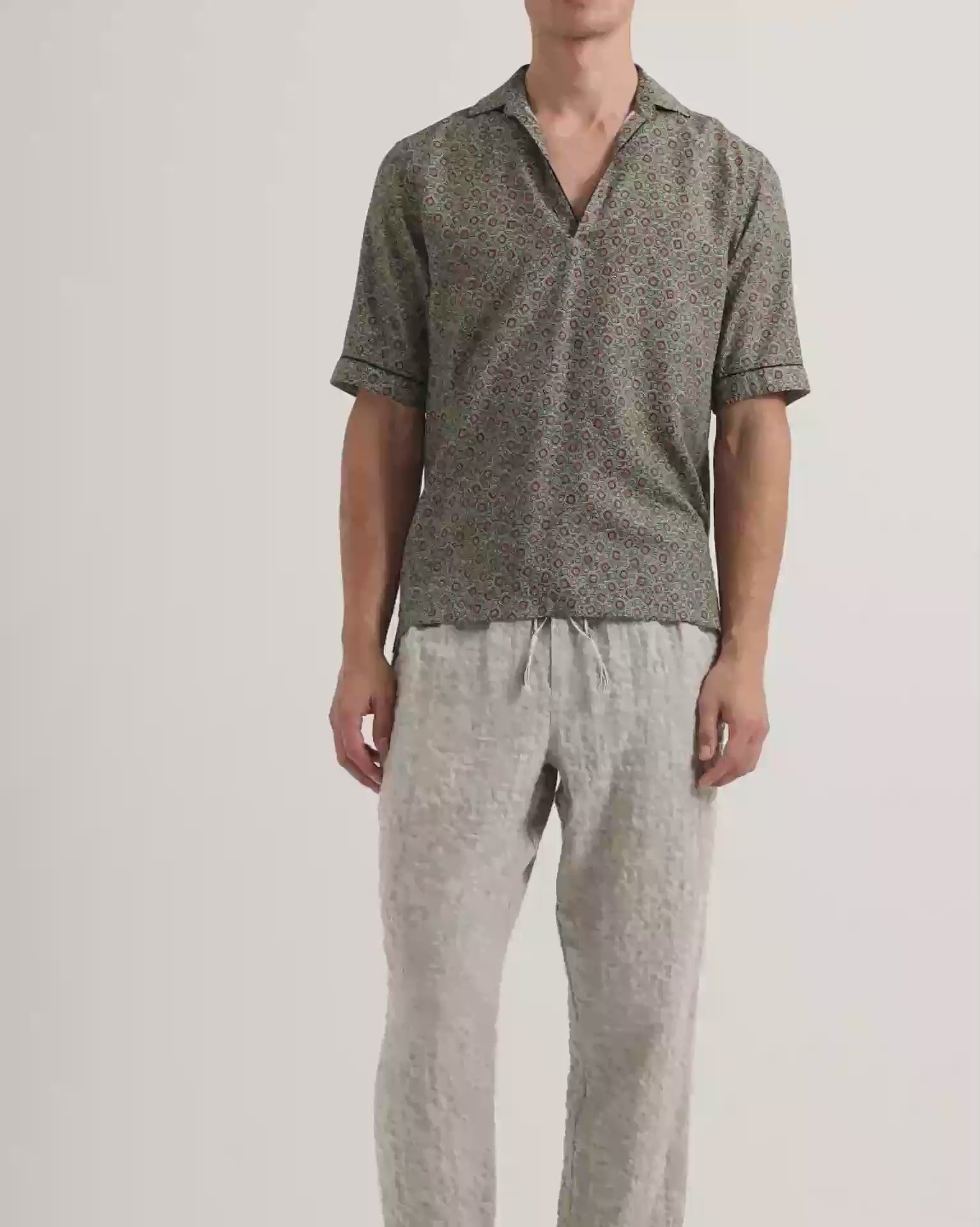 Man wearing patterned short sleeve shirt in green with light grey linen trousers