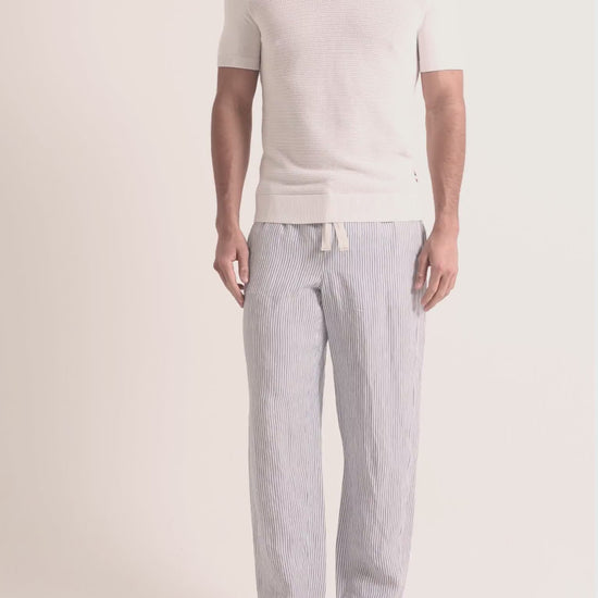 Man wearing white knitted polo shirt with blue striped trousers on a plain background