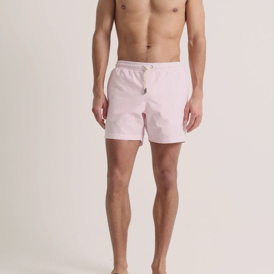 Man wearing pink seersucker swim shorts on a plain background