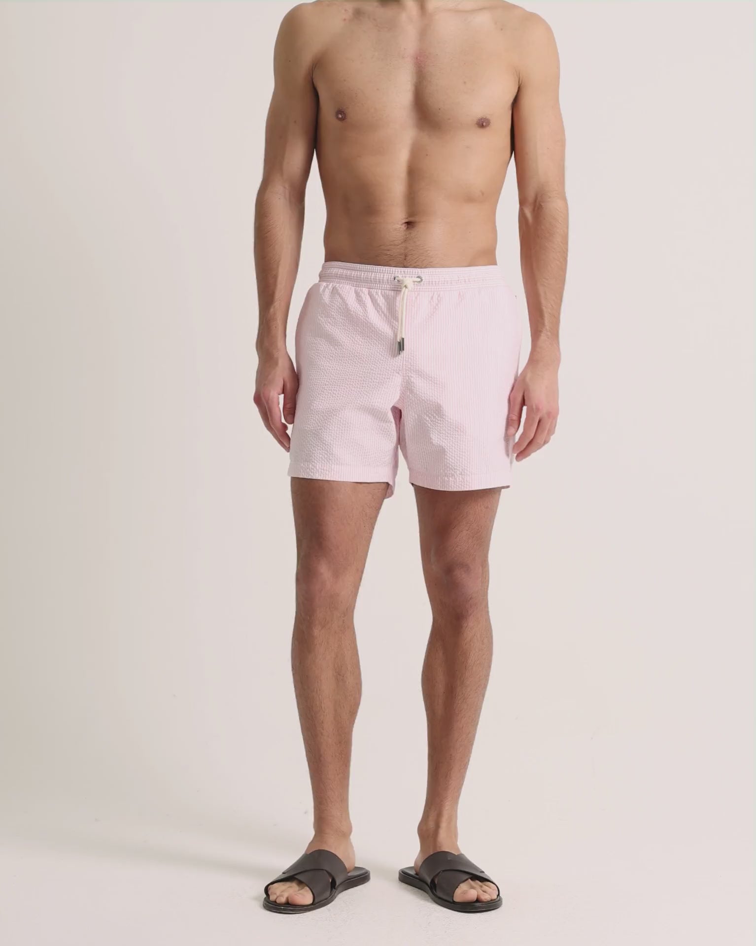 Man wearing pink seersucker swim shorts on a plain background