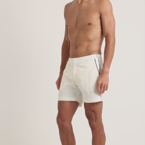 Man wearing white swim shorts with black trim detailing on a plain background