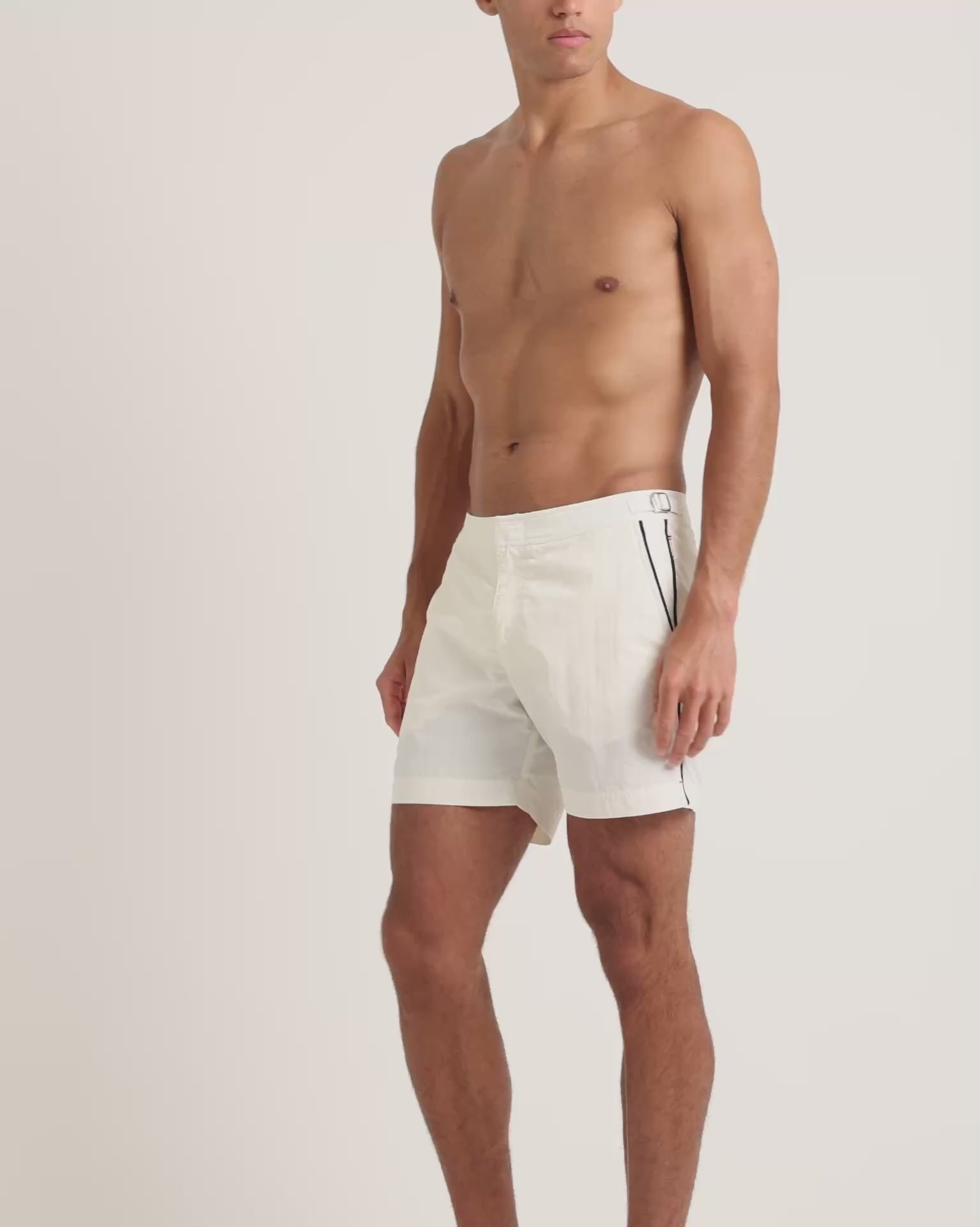 Man wearing white swim shorts with black trim detailing on a plain background