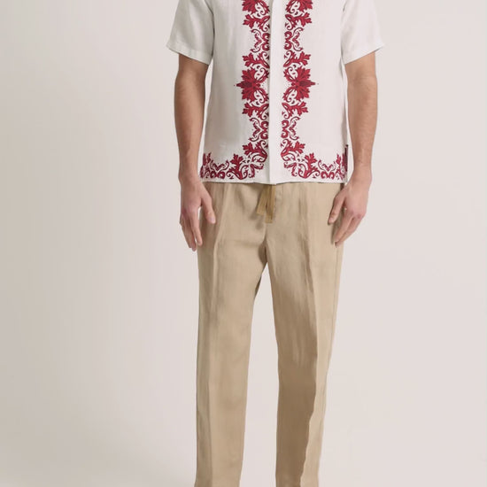 Man wearing printed white linen shirt with beige trousers on a plain background