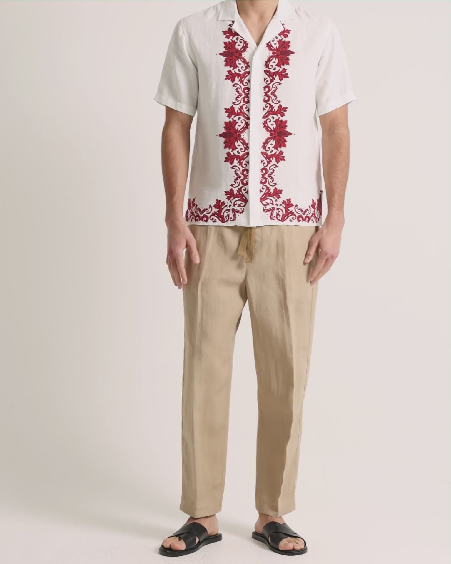 Man wearing printed white linen shirt with beige trousers on a plain background