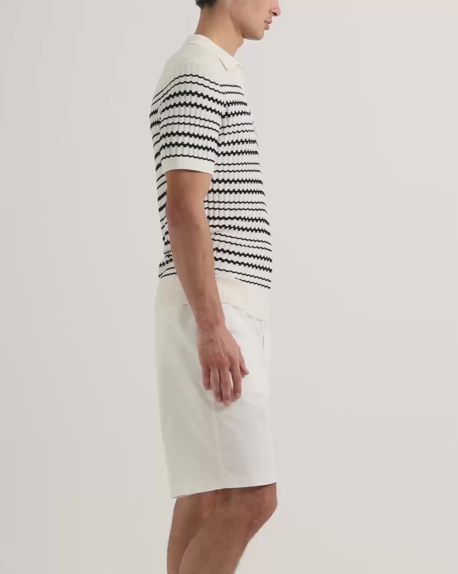Man wearing striped knitted polo shirt with white knee length shorts