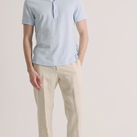 Man wearing blue polo shirt with beige linen trousers on a plain background