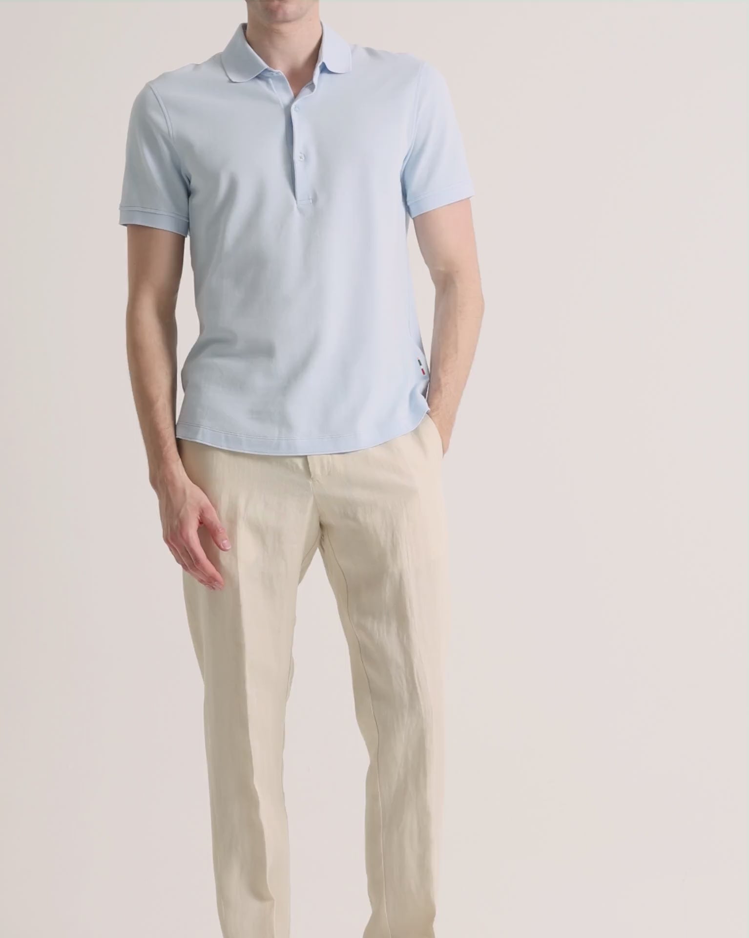 Man wearing blue polo shirt with beige linen trousers on a plain background