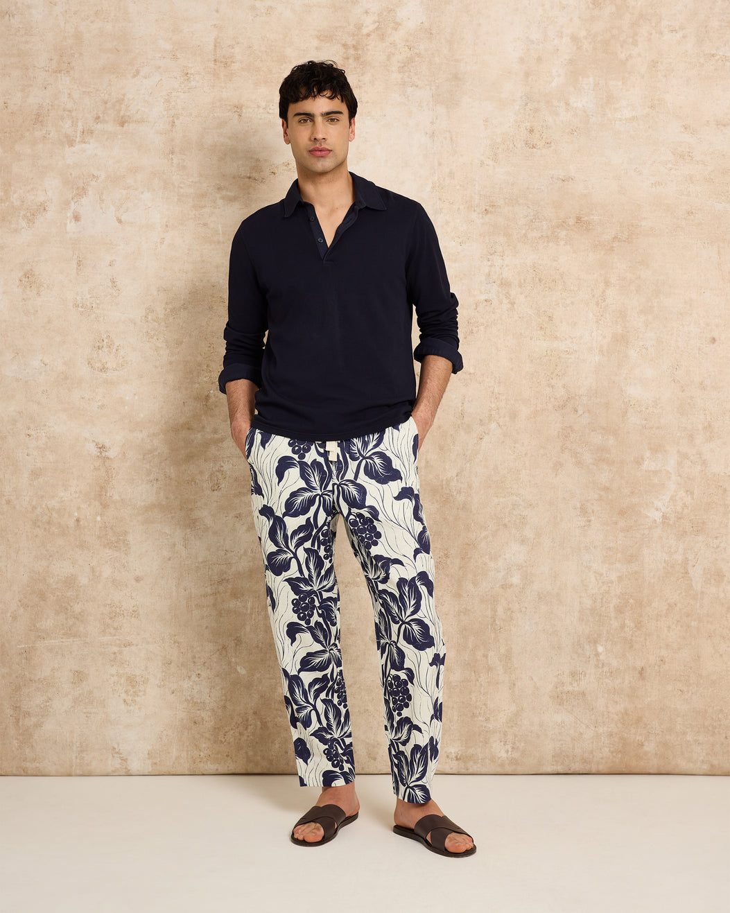 Man wearing a navy shirt and floral pants against a beige wall