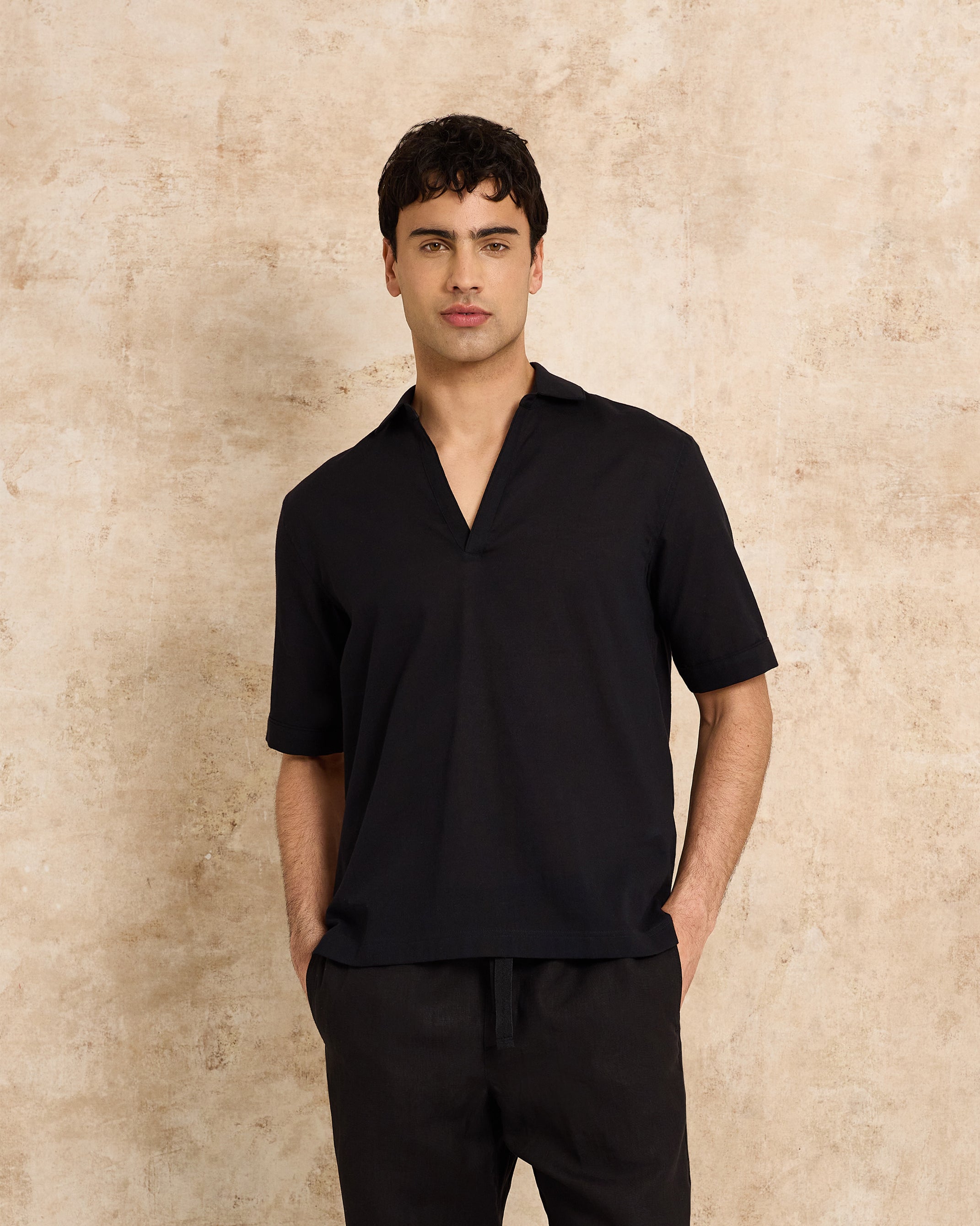 Man wearing a black shirt and pants against a beige wall