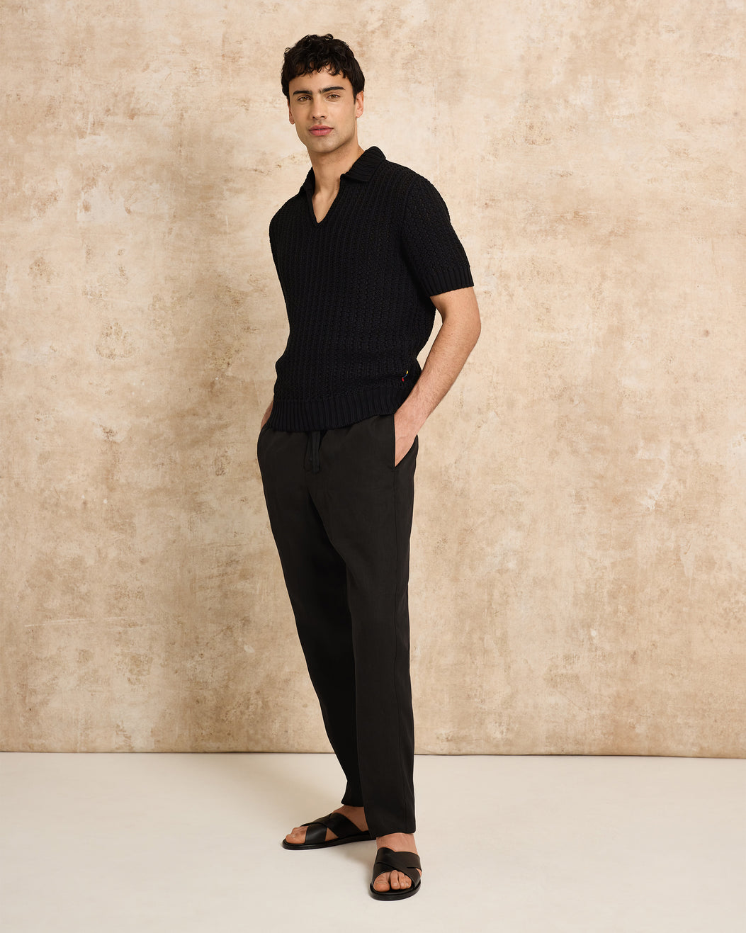 Man wearing a black polo shirt and pants against a beige wall