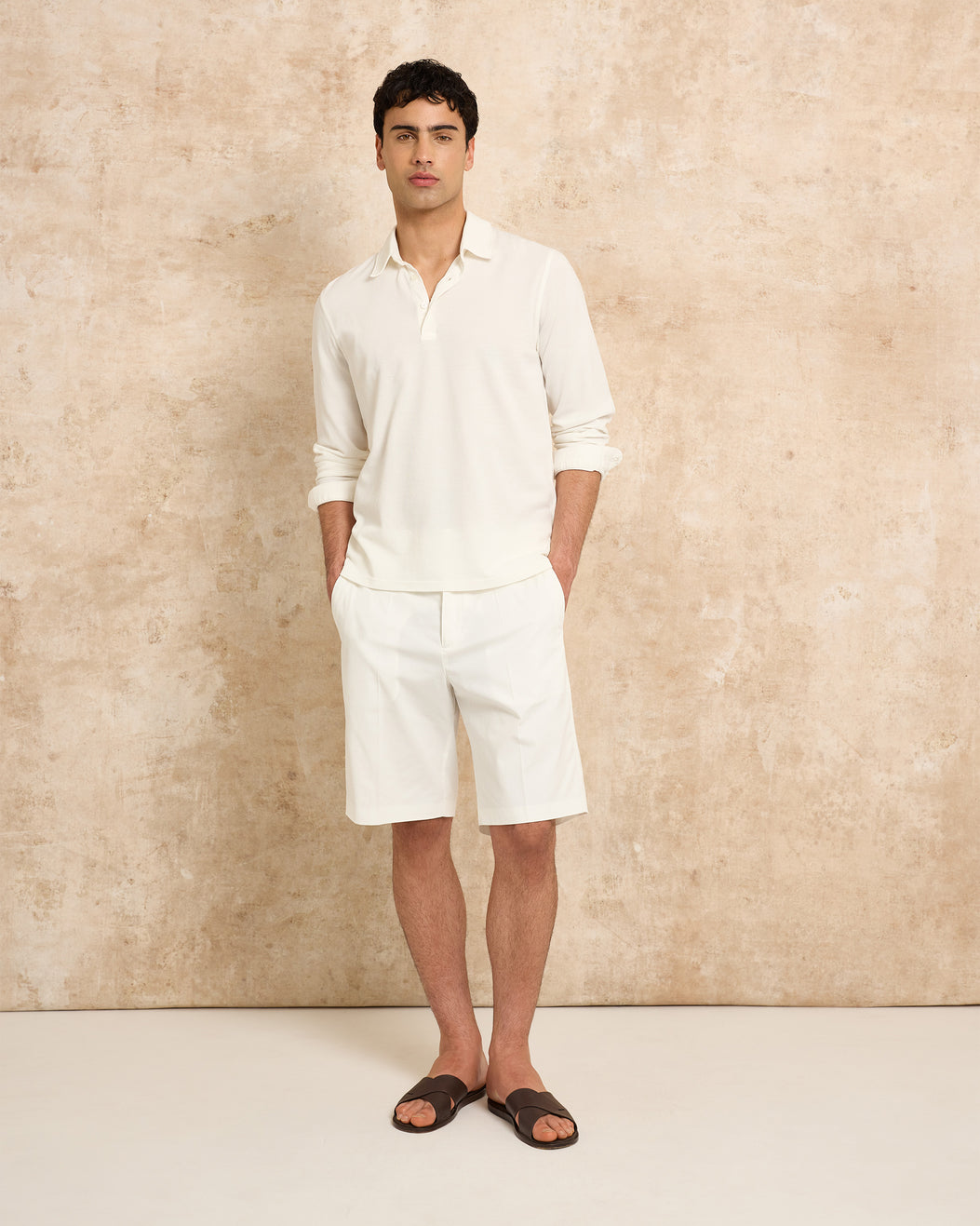 Man wearing a white polo shirt and shorts against a beige background
