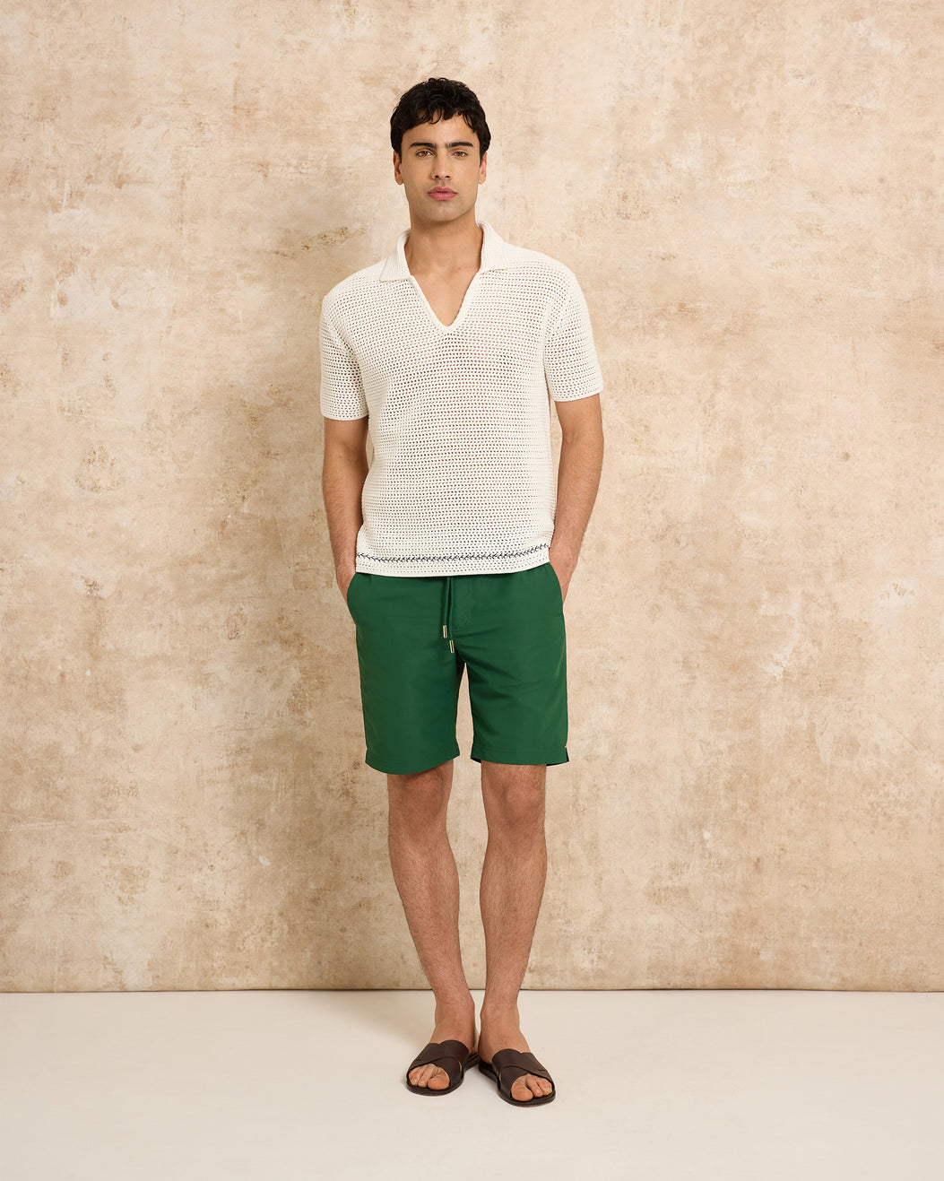 Man wearing a white textured shirt and green shorts against a beige background