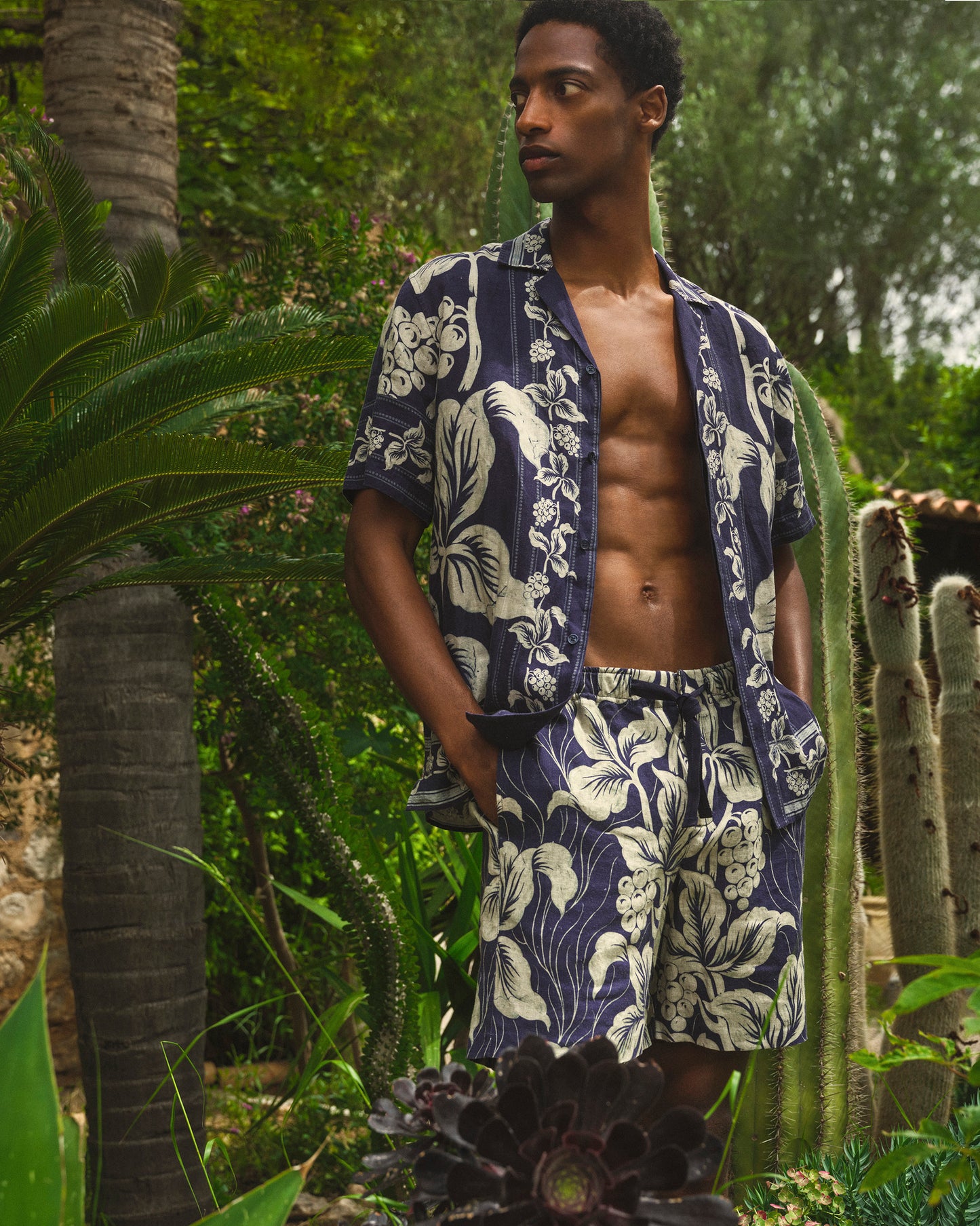 Man wearing a navy blue floral patterned shirt and shorts in a tropical setting with cacti and palm trees.