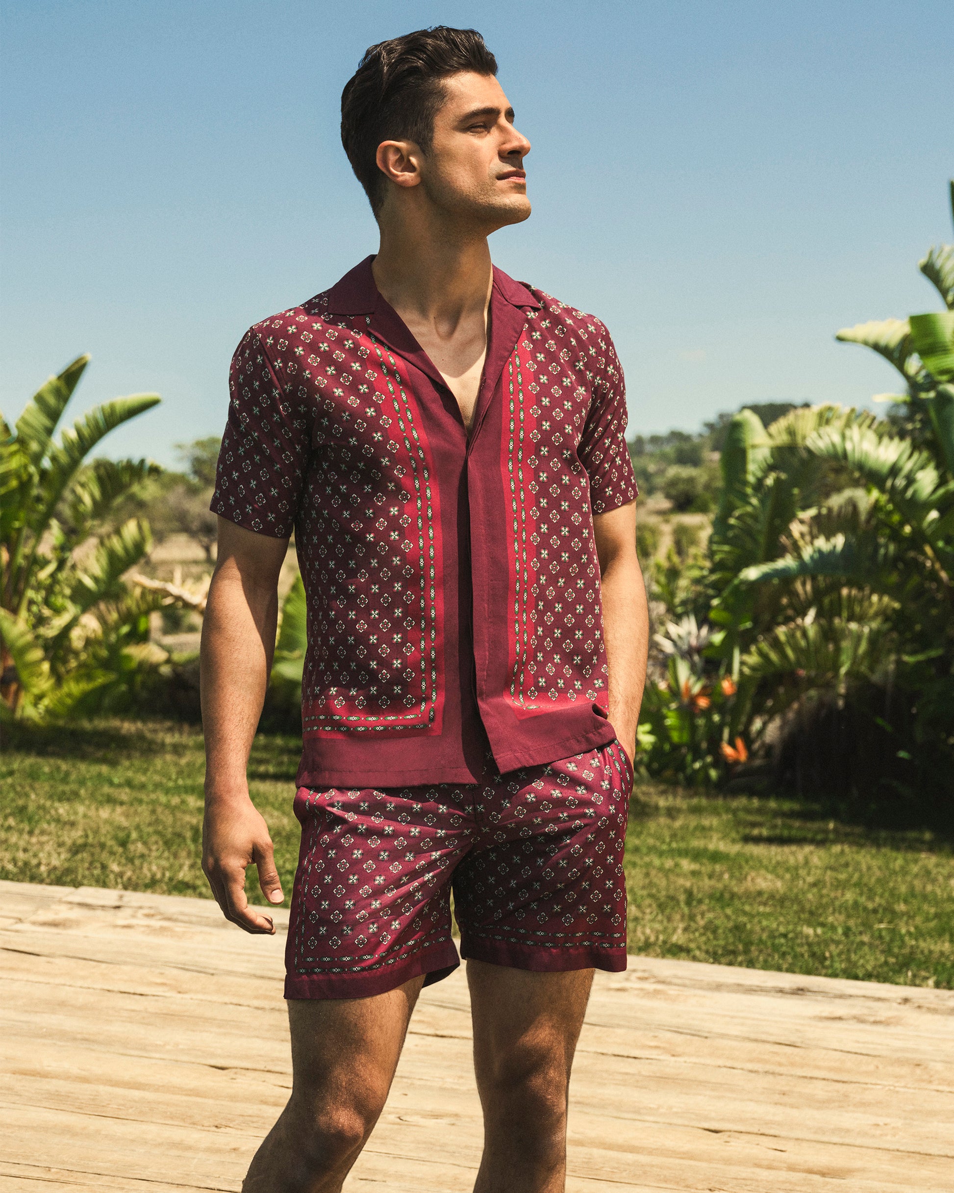 Man wearing a patterned outfit standing outdoors with greenery in the background