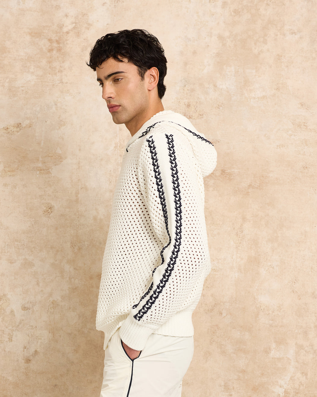 Man wearing a white textured sweater with black chain details against a beige background